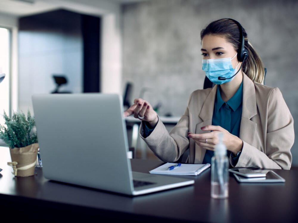 Businesswoman having conference call over laptop from the office Businesswoman with face mask making video call over laptop while working in the office.