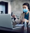 Businesswoman with face mask making video call over laptop while working in the office.