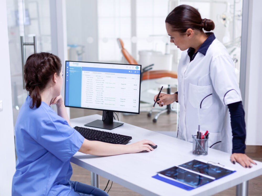 Stomatolog and nurse in tooth clinic checking patient appointment. Stomatolog and nurse in tooth clinic checking patient appointment looking at computer monitor. Stomatology assistant and teeth doctor discussing in reception of dental office
