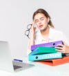 Young tired business woman with folders on office desk on white background